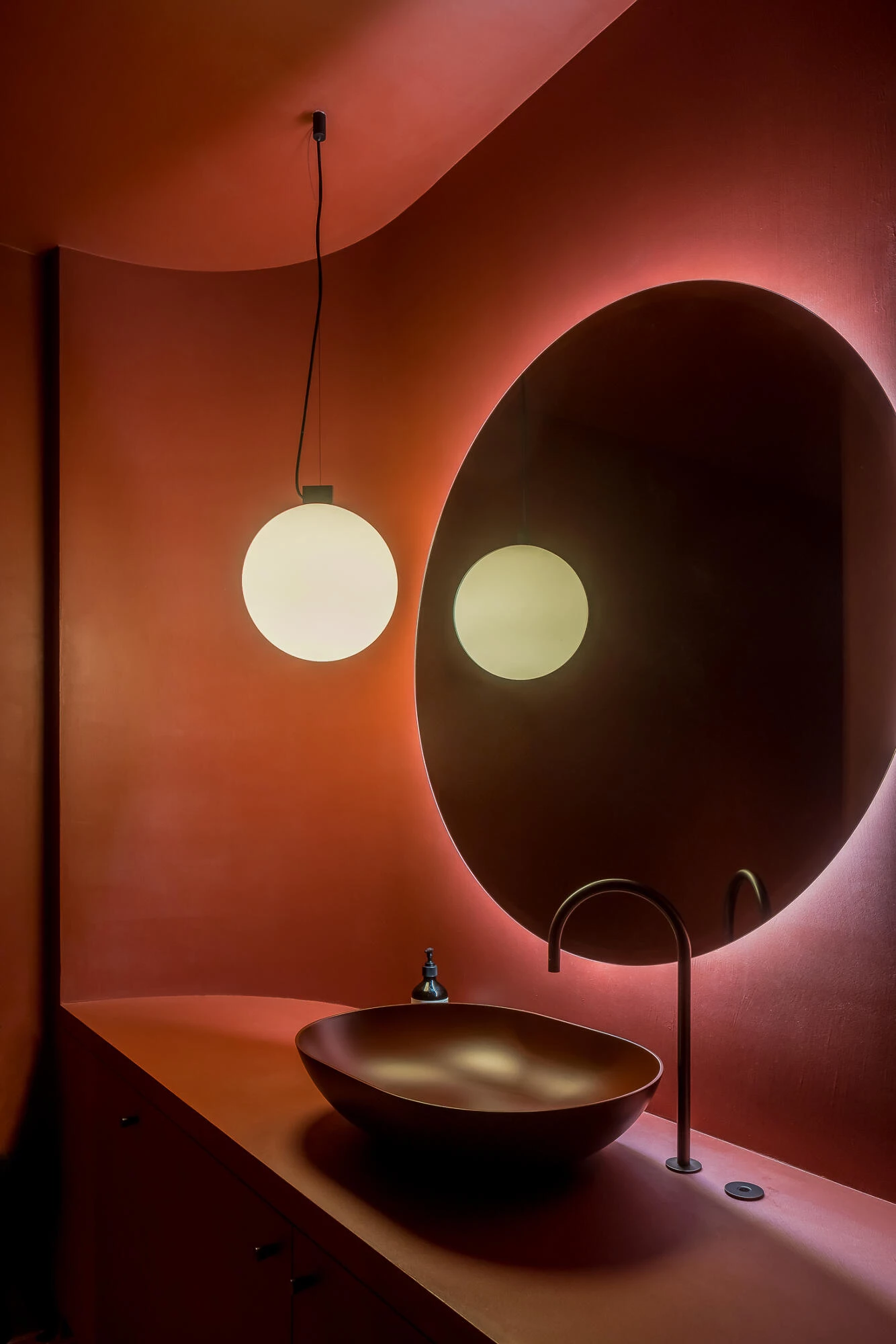 Wastafel toiletten in rode Socrete afwerking met ronde spiegel en designlamp
